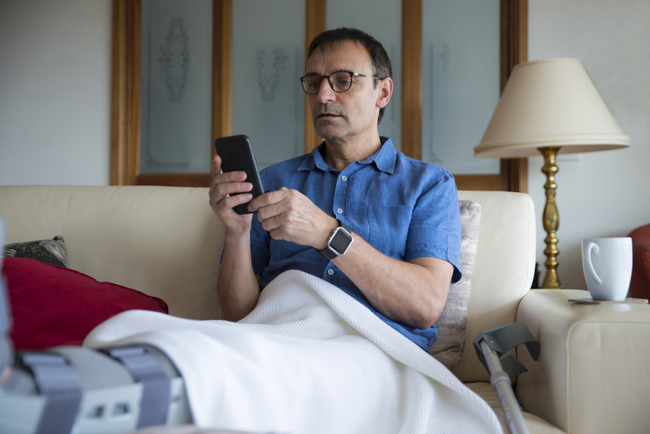 Photo of a man talking on the phone and resting. His leg is in a cast