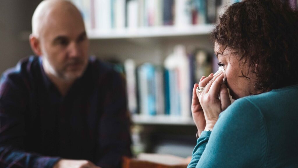 Photo of a man consoling a woman who is wiping away her tears with a tissue